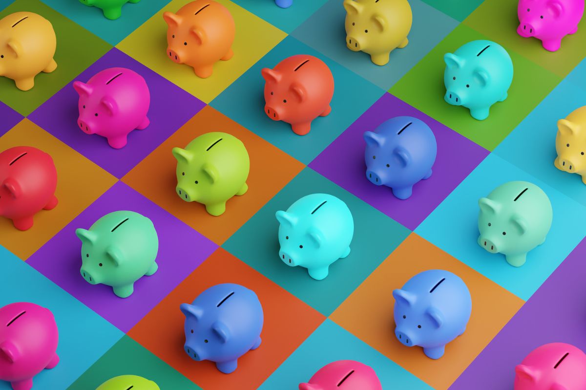 Mehrere bunte Sparschweine stehen auf einem farbigen Schachbrettmuster aus quadratischen Flächen in verschiedenen Farben.