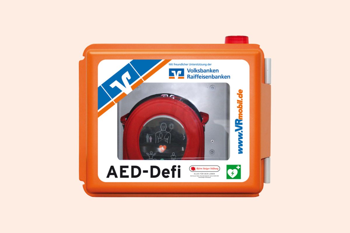 Orangefarbener Wandkasten mit einem automatisierten externen Defibrillator (AED), der für Notfälle mit Herzstillstand bereitsteht.