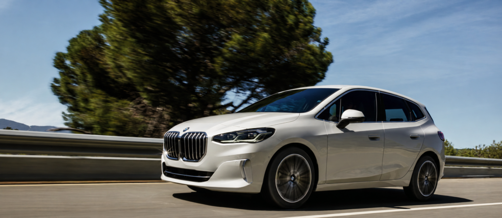 BMW weiß fahrend auf einer Straße mit Bäumen im Hintergrund